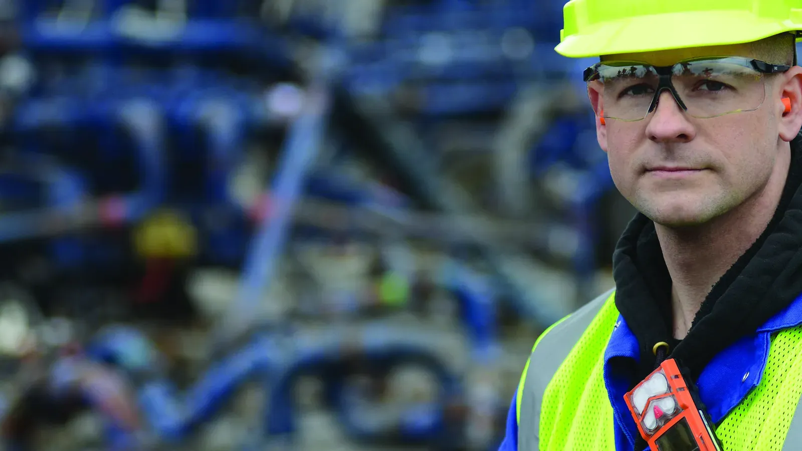Industrial Scientific field service worker in high-visibility PPE and safety glasses in a treatment-plant environment, the typical operator who carries a Ventis Pro5 personal multi-gas monitor
