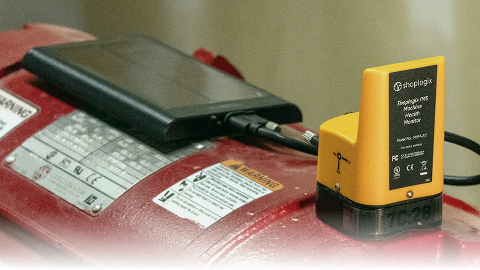 Everactive MHM 2.0 batteryless wireless vibration sensor mounted on the housing of a red industrial motor next to a small display unit and the motor's warning and rating labels